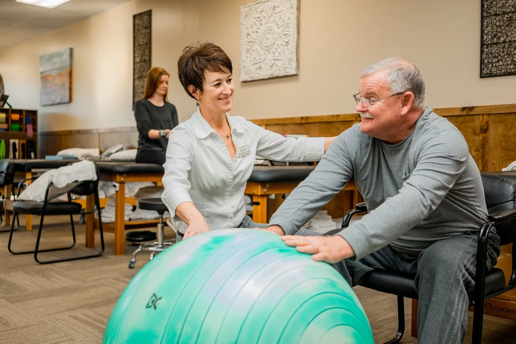 ApexNetwork Physical Therapist working on rehabilitation of a patient sitting in front of a large rubber ball.